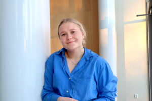 Foto av leende blond ung kvinna klädd i en klarblå skjorta.