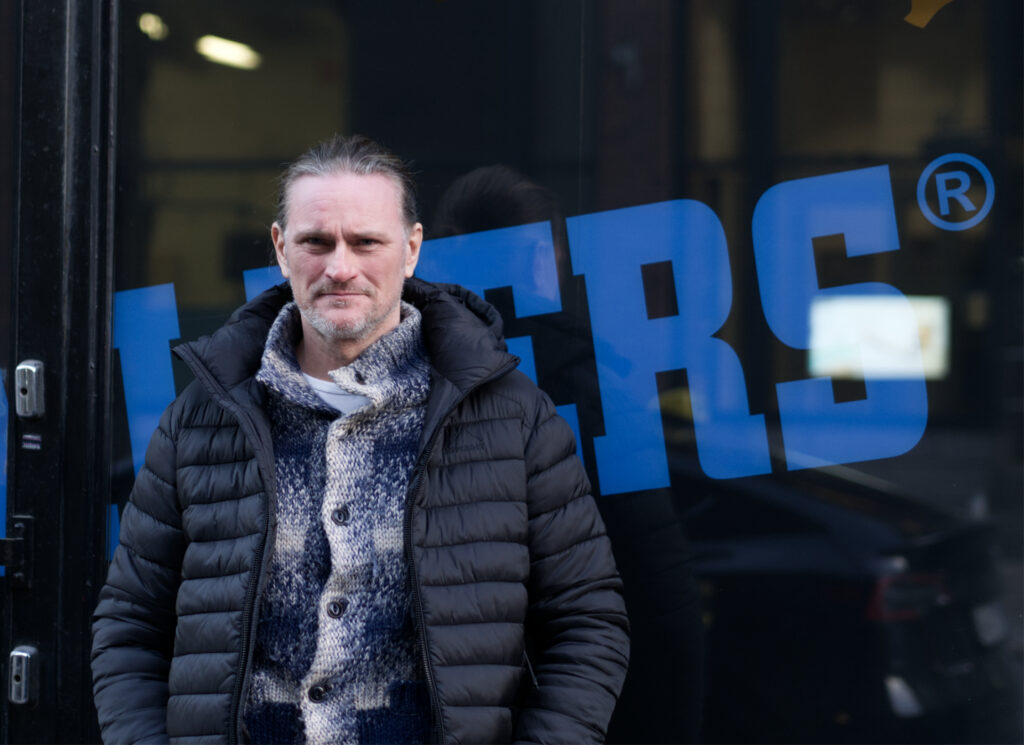 Man med mörkblå vinterjacka står lutad mot ett fönster som det står Walkers på.