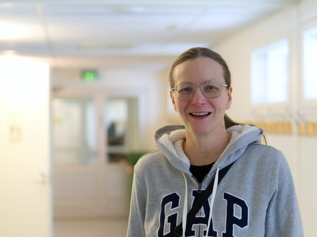 Leende kvinna med glasögon och brunt hår i en hästsvans. Hon är klädd i en grå GAP-huvtröja.