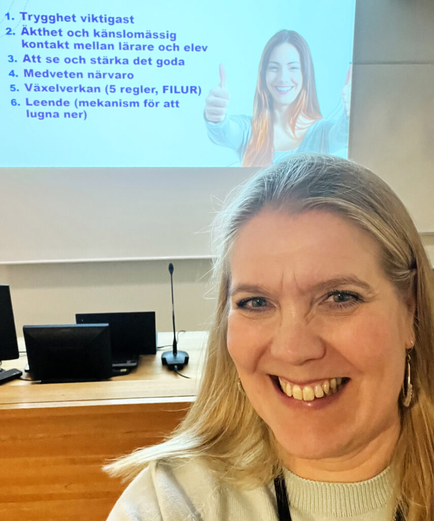 Kvinna med stort leende poserar framför en skärm där det står en lista med mobbningsförebyggande strategier.