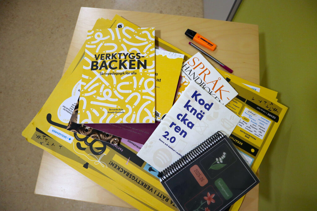 På bilden syns ett bord med olika slag av skolmaterial på. Här finns en kalneder med svart pärm och blommor, och böcker där det står Kodknäckaren 2.0, Verktygsbacken och Språkhandboken. DÄr ligger också en tusch och en understreckningspenna.