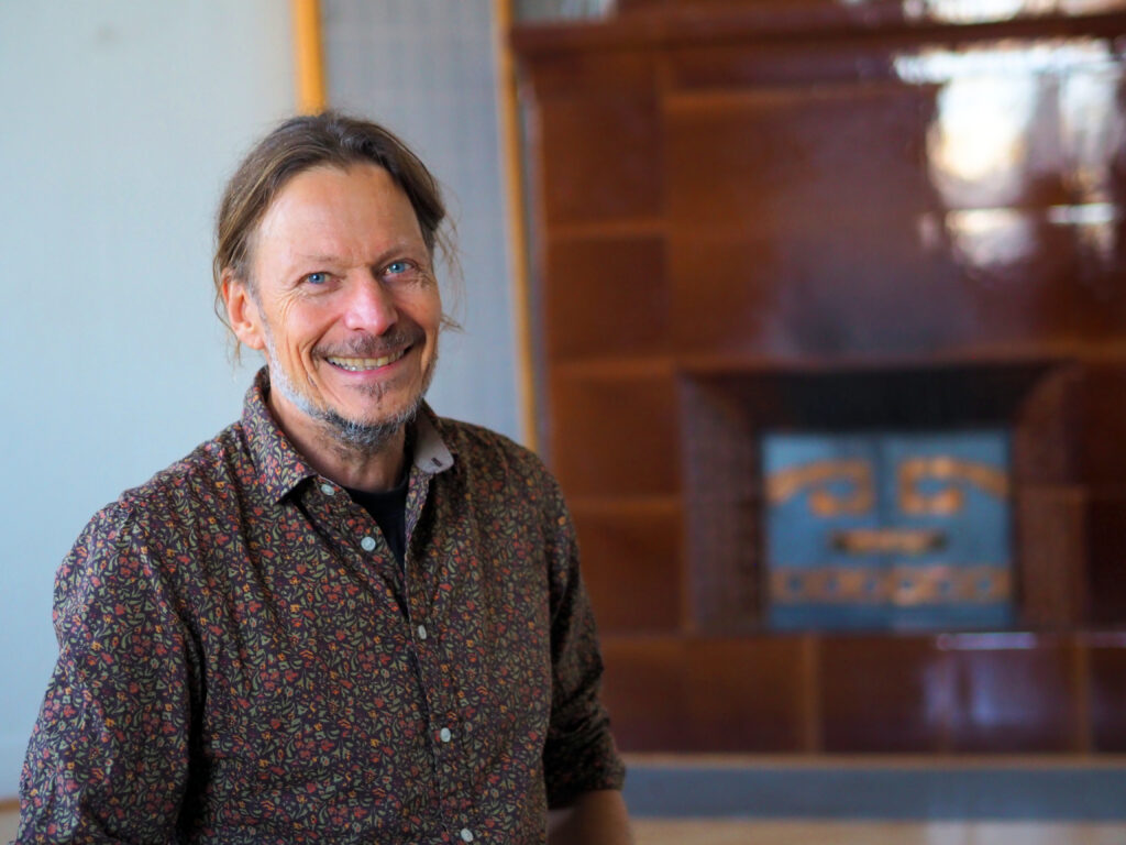 På bilden syns en medelålders man med blåa ögon, långt brunt hår i en knut i nacken och ett kort skägg som skiftar i vitt. Mannen, Vesa Puronkuru, är coach. Han är klädd i en brun skjorta med små röda blommor på. Han skrattar mot kameran. I bakgrunden kan man se en brun stor kakelugn.