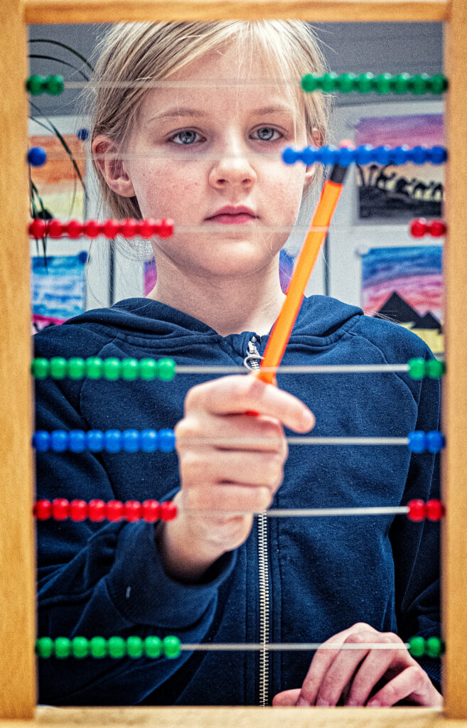 Flicka står och räknar med hjälp av en räkneram.