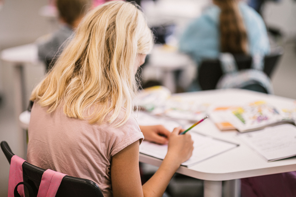 Flicka som sitter vid ett bord och skriver för hand i en arbetsbok.