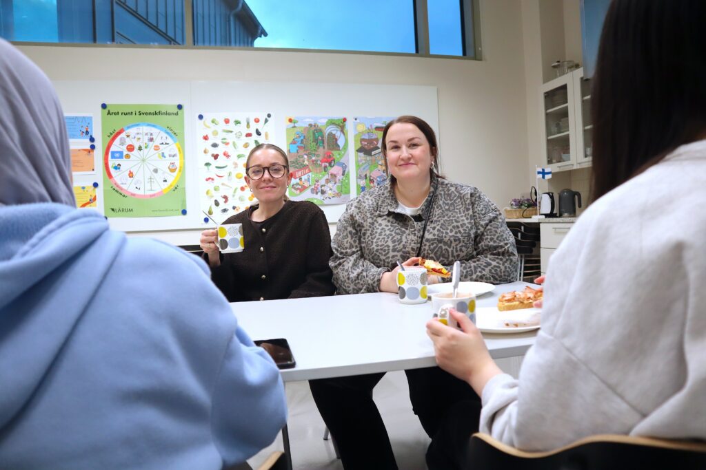 Två ledare sitter bredvid varandra i ett klassrum, och dricker kakao.