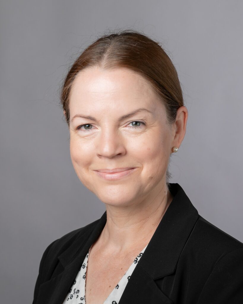 På bilden syns en medelålders kvinnan vid namn Minna Kyttälä. Hon har rödbrunt hår som är draget bakåt. Hon har gröna ögon, ljusrött läppstift och pärlor i öronen. Hon ser rakt in i kameran och har ett roat leende. Hon är klädd i en vit blus med svart mönster och en svart kavaj. Hon intervjuas om pedagogers arbetsvälbefinnande.