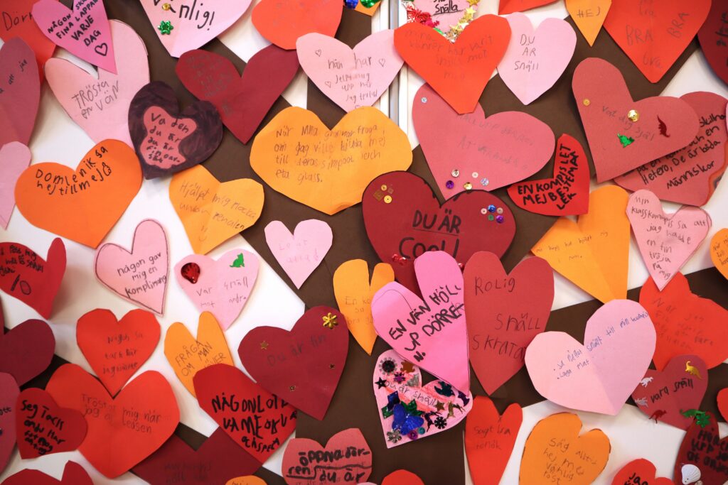 På bilden syns en massa kartonghjärtan i rött, orange och rosa med texten i svart och kulspets på. Där står positiva saker som Du är cool eller En vän höll upp dörren.