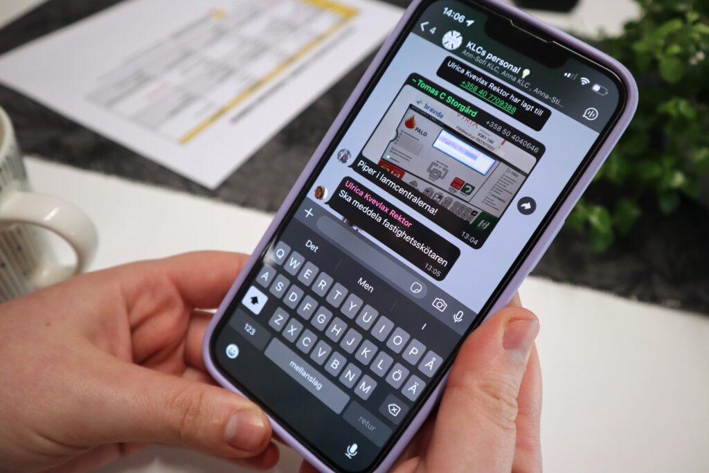 På bilden ser man två händer som håller i en mobiltelefon som har ljuslila längs kanterna. På mobilen ser man tangentbordet nertill och några meddelanden med en bild på mitten.