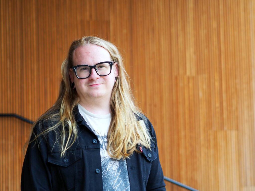 På bilden syns en medelålders man med långt ljust hår som är utslaget. Han heter Eso Yli-Hemminki och talar om våld i skolan. Han har glasögon med mörka tjocka skalmar. Han ser rakt in i kameran och ser glad ut. Hon är klädd i en vit t-shirt med tryck i grått framtill och har en mörkblå jeansjacka ovanpå. Bakgrunden är en vägg i rödbrunt trä i smala paneler.