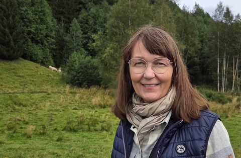 På bilden syns en medelålders kvinna vid namn Gunilla Karlberg-Granlund som talar om att tolka läroplanen. Hon har brunt axellångt hår med pannlugg. Hon har glasögon med tunna ljusa bågar, hon tittar rakt in i kameran och ler så man ser tänderna. Hon har en beige scarf, en mörkblå vadderad väst och en vit och grå skjortblus under. I bakgrunden ser man gräs och träd.