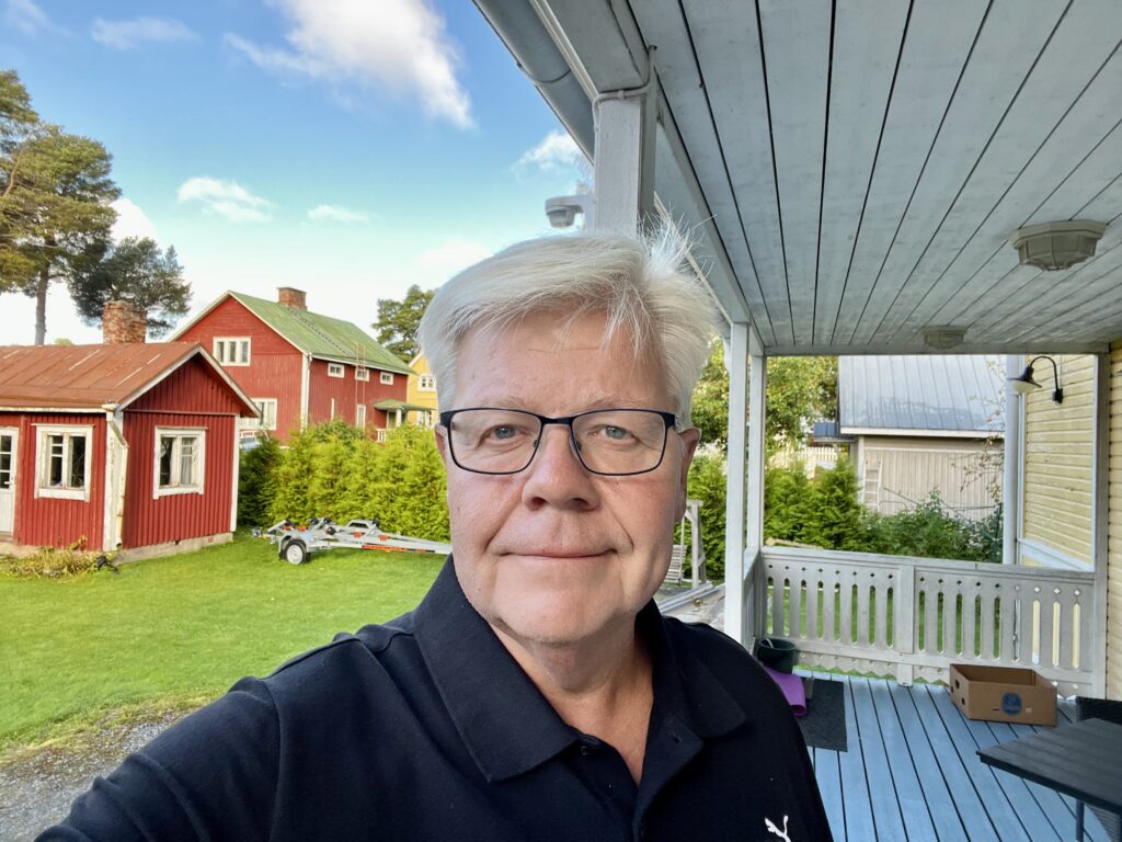 På bilden syns en åäldre man vid namn Michael Uljens som talar om lärarnas autonomi. Han är centrerad mitt i bilden, ser rakt in i kameran och har en neutral min. Han har vitt hår, glasögon med tunna mörka bågar och är klädd i en mörkblå t-shirt med krage. I bakgrunden ser man till vänster två små röda hus och en gräsmatta med en båttrailer på. Till höger finns en verande med vitt ta, pelare och staket somt ljusblått golv.